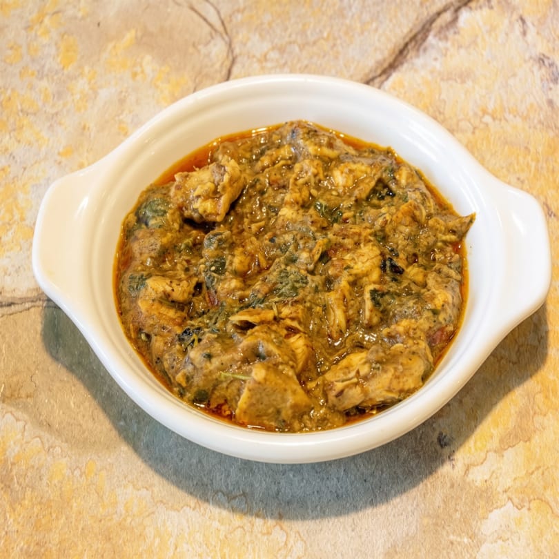 A white oval dish filled with a rich, chunky brown and green stew, possibly chicken or meat.