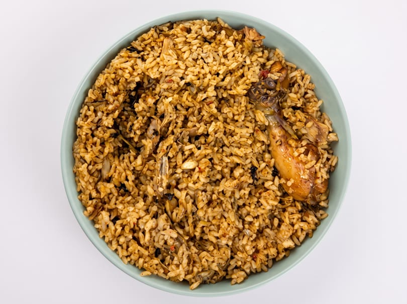 Overhead view of a light blue bowl filled with chicken and rice, on a white background.